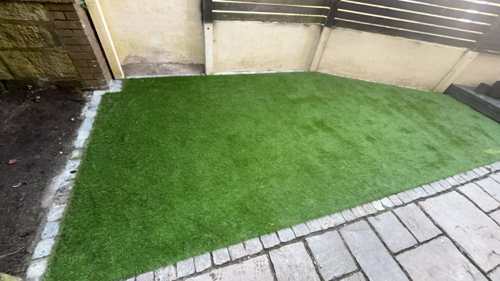 Artificial grass fitted up to a rendered wall and fencing in Kilwinning.