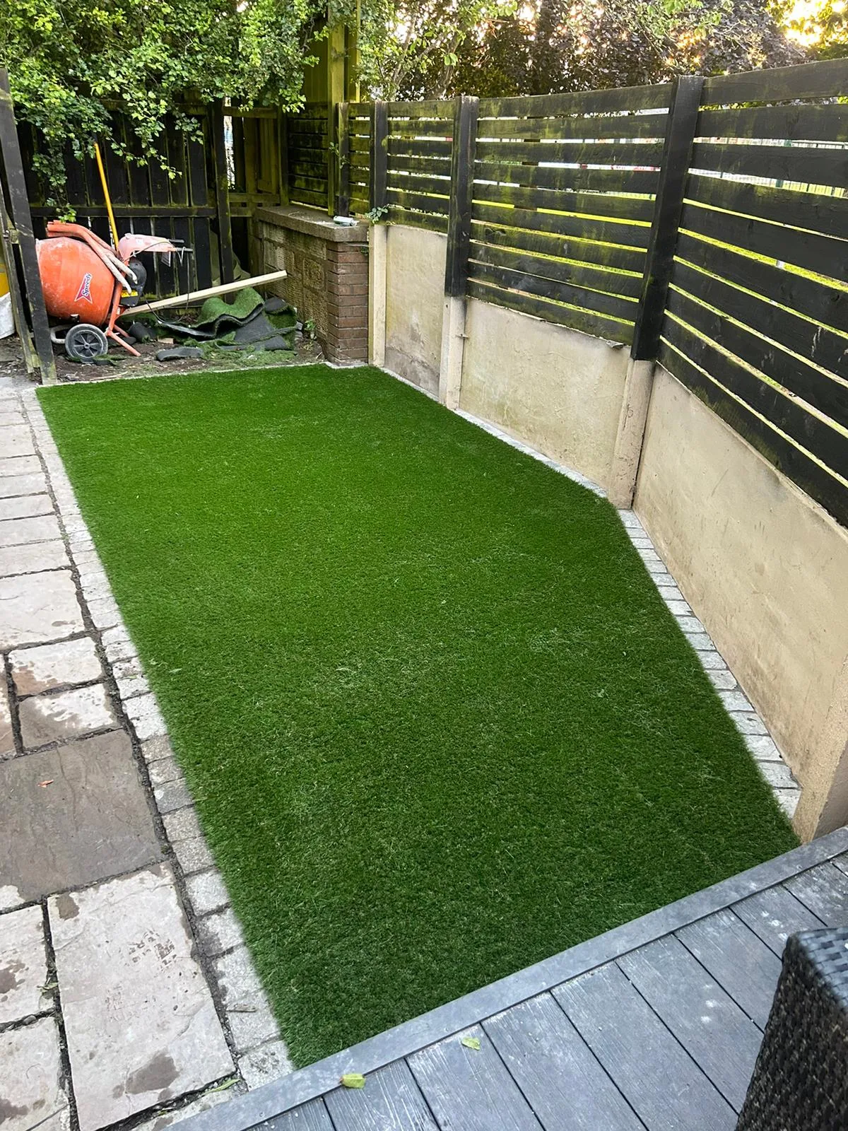 Artificial grass lawn fitted tight to a paved border in an enclosed back garden.
