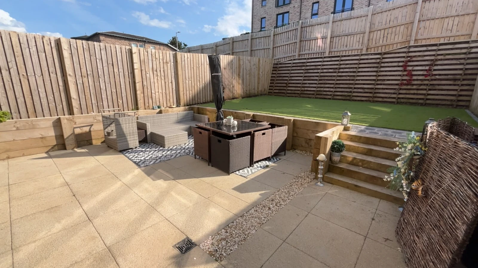 Sleeper retaining walls and steps beside a paved patio and raised artificial grass lawn.