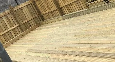 Newly laid timber decking boards with a feather-edge fence behind.