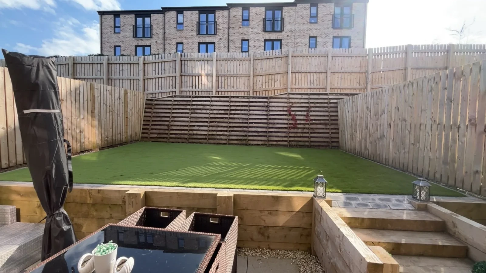 Sleeper steps leading from a paved patio to a raised artificial grass lawn at the Greenock luxury townhouses.