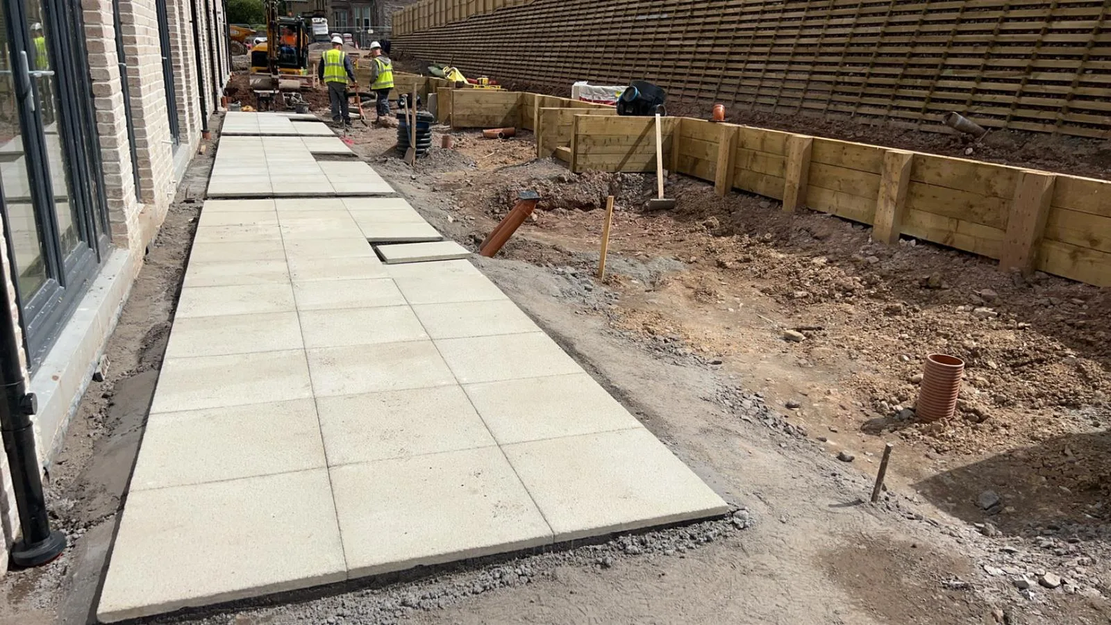 Paving slabs being laid beside a new-build home at the Greenock luxury townhouse development, with a sleeper retaining wall under construction alongside.