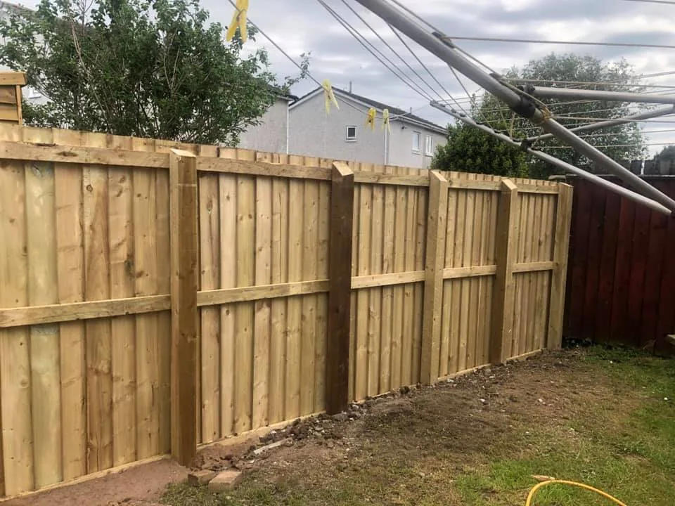 New closeboard timber boundary fence with posts and rails along the edge of a lawn.