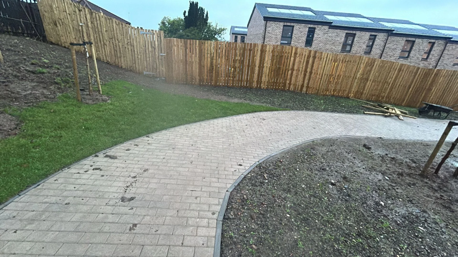 Curved monoblock path with kerb edging winding through a new garden at the Greenock luxury townhouse development, with new timber fencing and turf alongside.