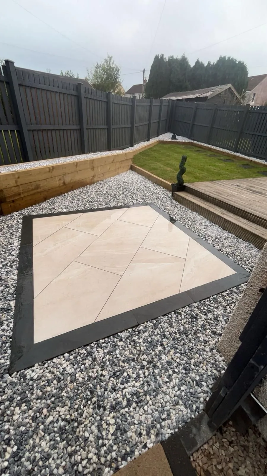 Decking steps beside a porcelain patio with a dark border and stone chips.