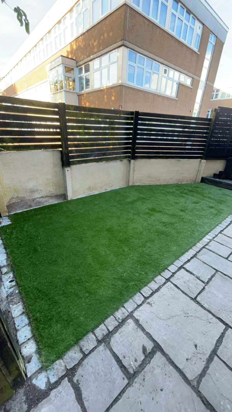 Artificial grass lawn beside a paved patio and slatted fencing in Kilwinning.