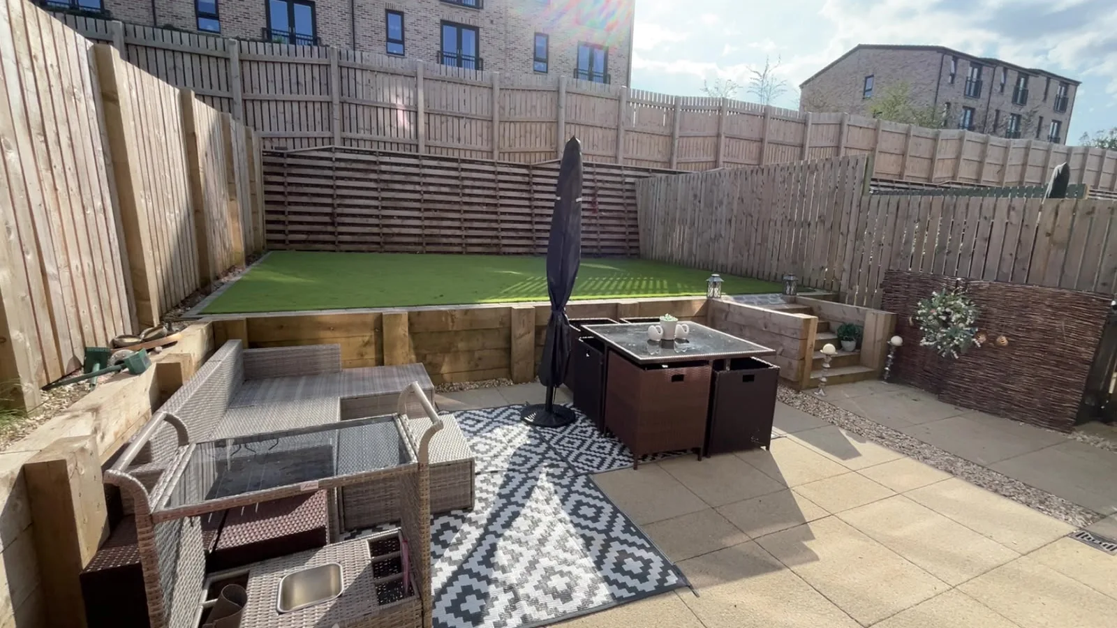 Garden with artificial turf, sleeper retaining walls and a paved patio.
