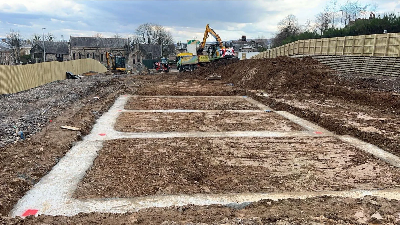 Strip foundations dug out and filled with concrete on a new-build site, with the trench runs marked out ready for blockwork.